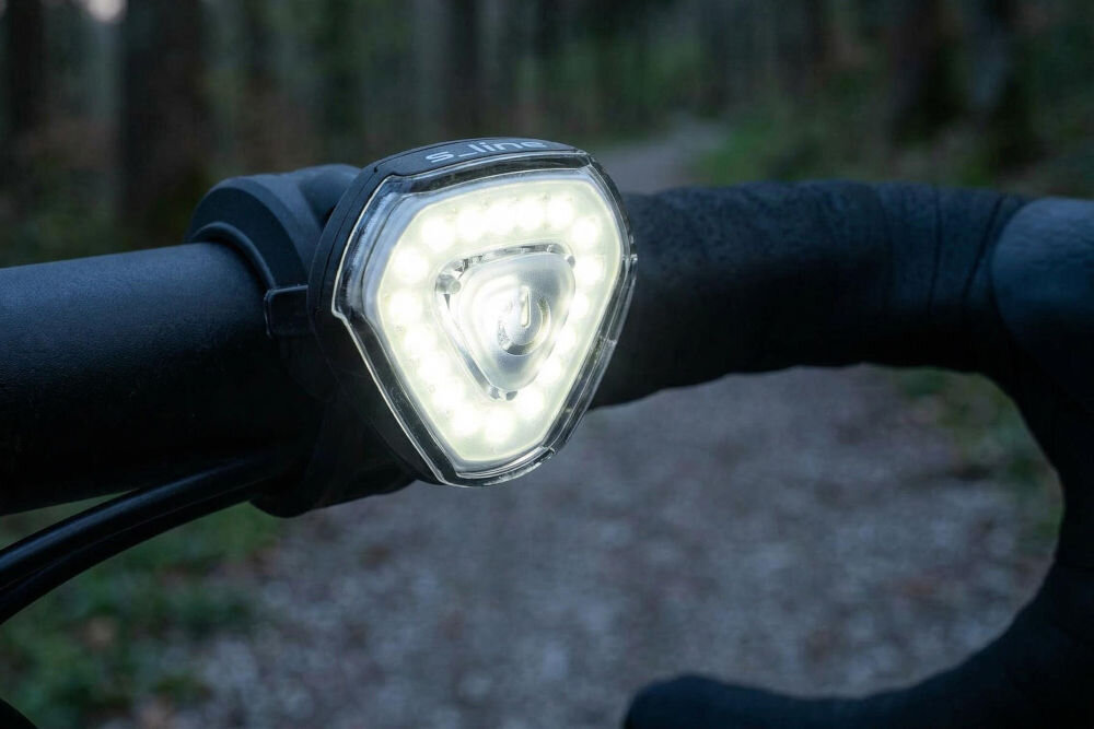 Zestaw lampek rowerowych S-LINE BL605 Widok z tyłu na rowerzystę w lesie z włączoną czerwoną lampką tylną S-LINE zamontowaną pod siodełkiem, zapewniającą widoczność po zmroku.