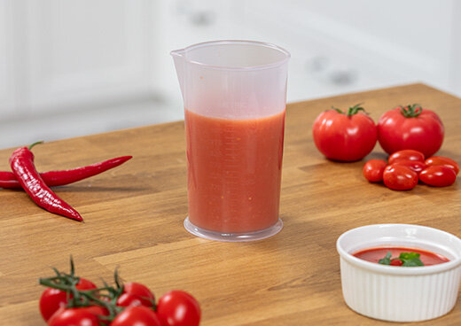 Miarka wypełniona zblendowanym sosem pomidorowym na drewnianym blacie. Obok pomidory i papryczki.