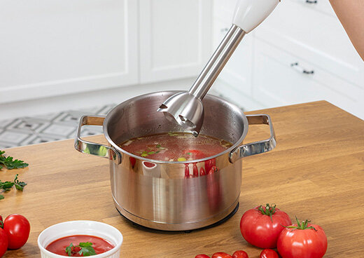 Blender ręczny MBL-43 nad garnkiem z zupą. Obok pomidory na blacie kuchennym pomidory.