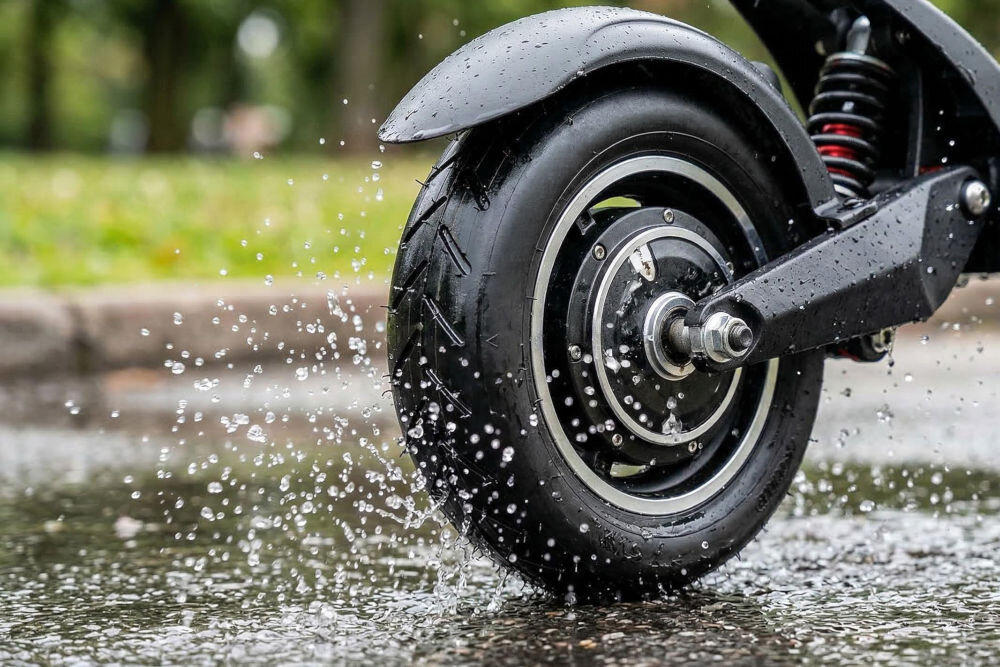 Opona S-LINE EST8503 8.5 cala Zbliżenie na tylne koło hulajnogi elektrycznej jadącej po mokrej nawierzchni. Opona S-LINE skutecznie odprowadza wodę, tworząc wyraźne rozbryzgi spod błotnika.
