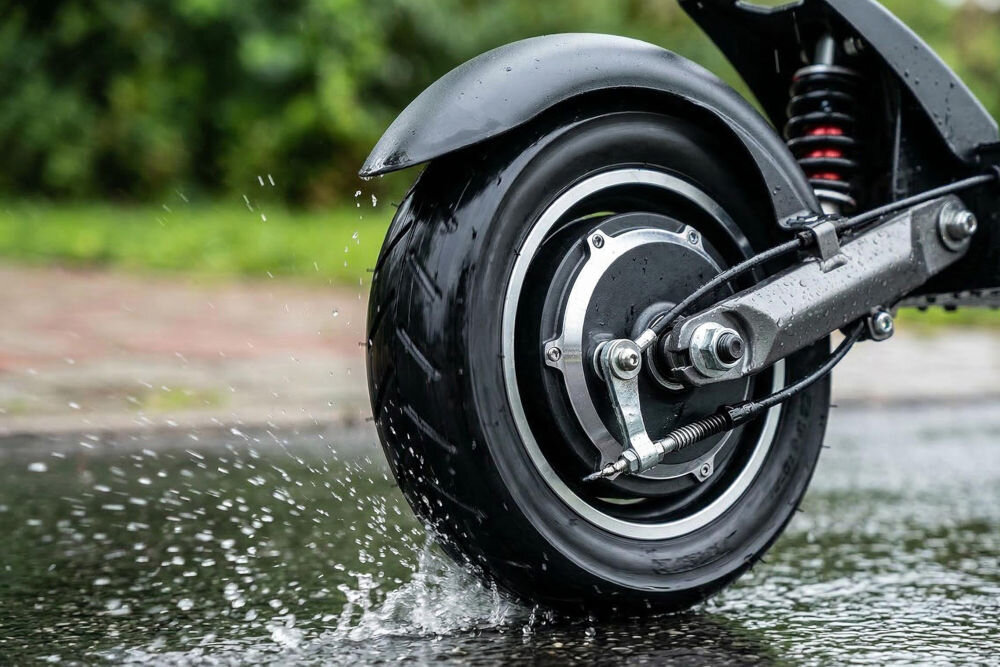 Opona S-LINE EST8503 8.5 cala Koło hulajnogi elektrycznej w ruchu na mokrym asfalcie. Widoczna praca bieżnika opony S-LINE i amortyzacja podczas jazdy w deszczowych warunkach.