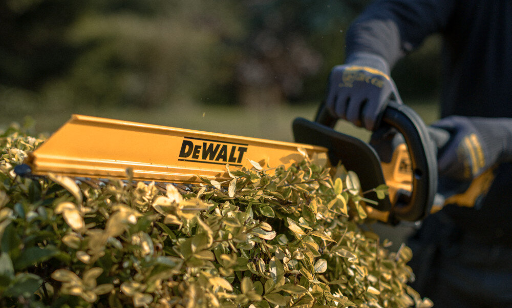 Nożyce do żywopłotu DEWALT DCMHT564P1-QW 550mm 18V akumulatorowe ogród osoba przycina żywopłot na ostrzu ma założoną osłonę do zbierania liści kompatybilność z osłoną do zbierania ściętego żywopłotu DEWALT® usuwanie odciętych gałązek ułatwia zachowanie porządku ogranicza konieczność późniejszego grabienia i skraca czas sprzątania