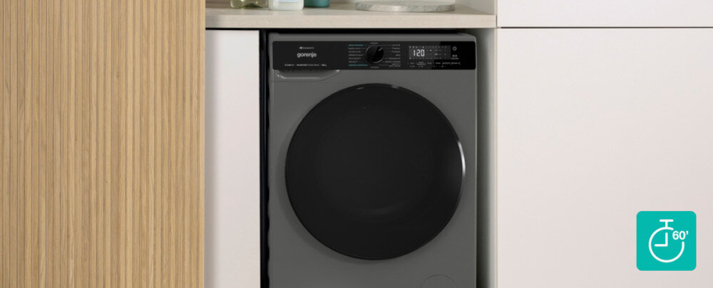 Pralko-suszarka GORENJE G600 WD2PA964ADT/PL Ciemnoszara pralko–suszarka z dużymi, przyciemnianymi drzwiami została elegancko zabudowana między białymi frontami i pionowym panelem z jasnego drewna. W prawym dolnym rogu znajduje się turkusowa ikonka zegara z oznaczeniem „60’”, sugerująca szybki, godzinny program prania lub prania‑suszenia pranie suszenie jeden cykl oszczędność czasu szybkie odświeżanie mały wsad codzienna odzież