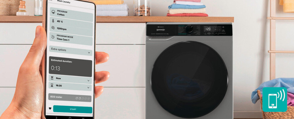 Pralko-suszarka GORENJE G600 WD2PA964ADT/PL Na zdjęciu widać pralko–suszarkę sterowaną z poziomu smartfona – z lewej strony ręka trzyma telefon z aplikacją pokazującą ustawiony program prania, temperaturę, prędkość wirowania i czas do końca cyklu. Po prawej stoi ciemna pralka z dużymi, przyciemnianymi drzwiami, a w dolnym rogu umieszczono turkusową ikonkę smartfona z falami sygnału, podkreślającą funkcję zdalnej łączności ConnectLife aplikacja zdalne sterowanie pralko-suszarka kontrola telefonu powiadomienia wygoda oszczędność czasu
