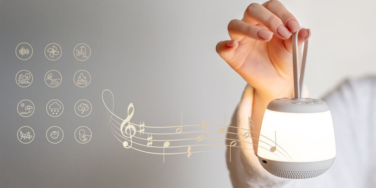 Lampka nocna LED NEWELL SeleneDream NL4496, relaks, dźwięki, natura, kołysanki, Kobieca dłoń trzyma za uchwyt zapaloną SeleneDream. Na zdjęciu takżę grafika pięciolinii z nutami i ikonami dźwięków.