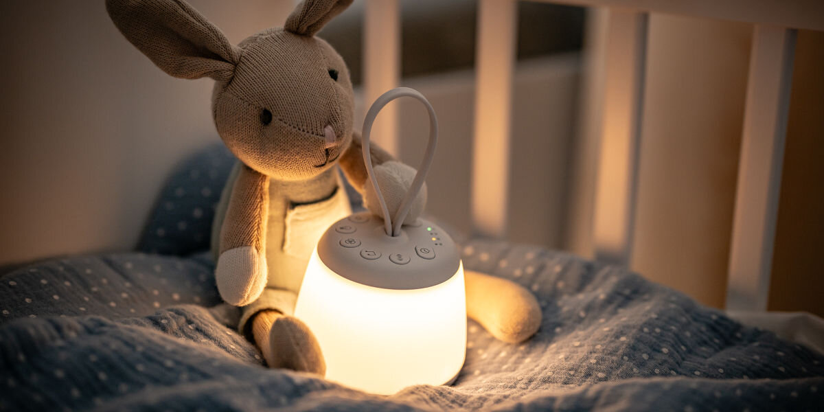 Lampka nocna LED NEWELL SeleneDream NL4496, mobilność, ładowanie, podróż, elastyczność, Klimatycznie świecąca lampka nocna Newell SeleneDream w dziecięcym łóżeczku na pościeli w kropki przy pluszowym króliczku.