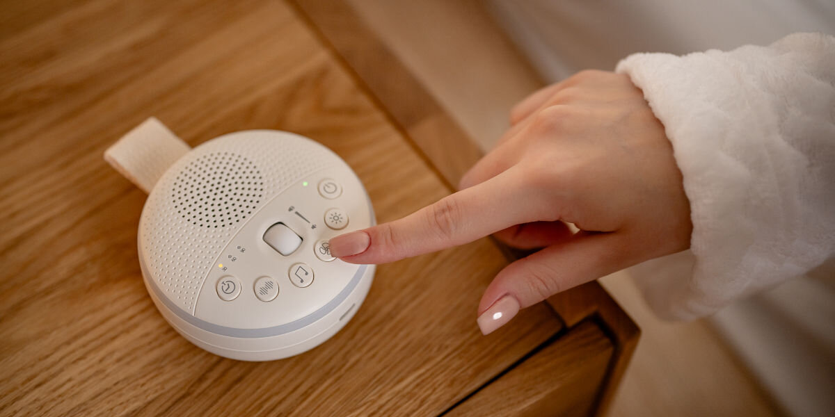 Lampka nocna LED NEWELL LunaWhisper NL4497, sterowanie, ustawienia, ergonomia, pamięć, lampka leży na szafce nocnej, palec dłoni wciska jeden z przycisków lampki