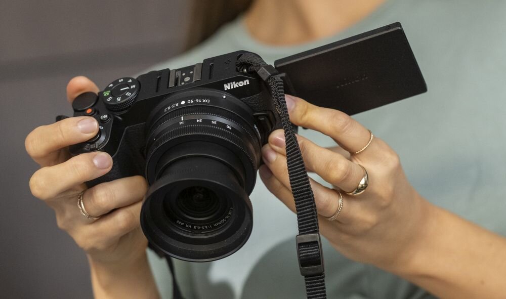Osoba trzyma aparat bezlusterkowy z obiektywem, na którym widoczny jest napis \'Nikon\'.