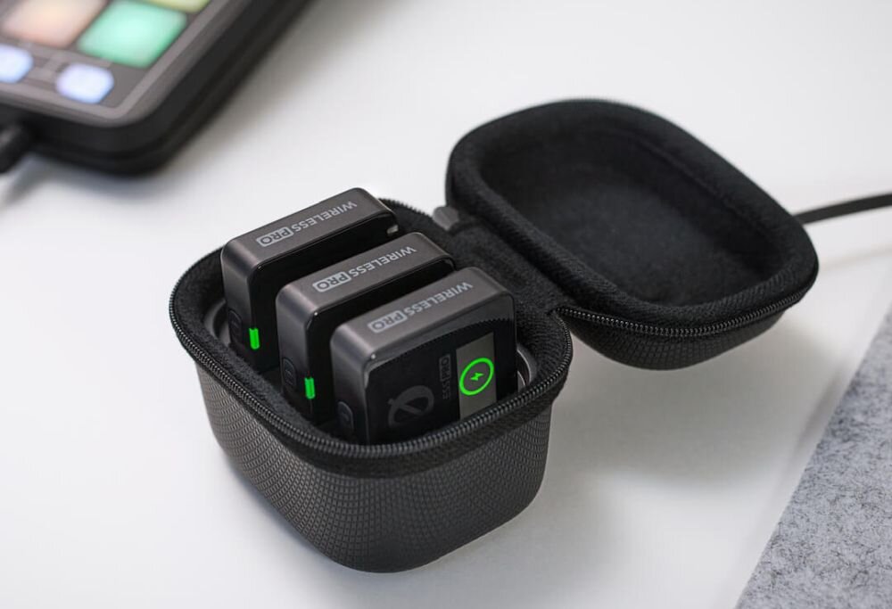 Na obrazie widoczny jest otwarty futerał z trzema urządzeniami oznaczonymi jako \'Wireless Pro\', z zielonymi wskaźnikami świetlnymi. Obok znajduje się fragment urządzenia z kolorowymi przyciskami.