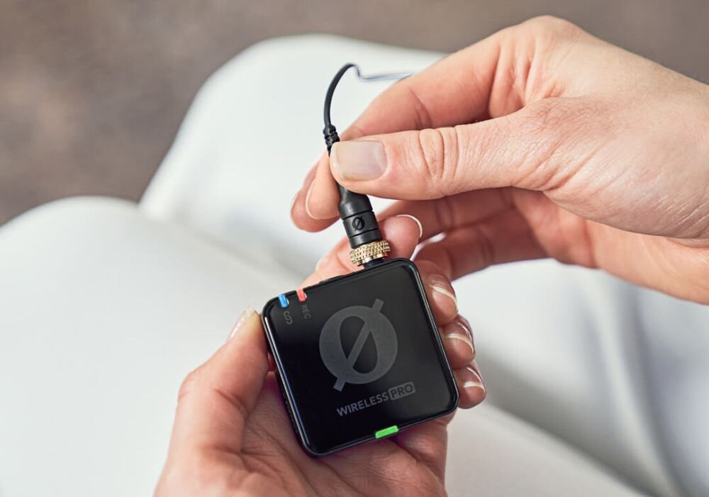 Osoba trzyma czarny, kwadratowy moduł z napisem \'WIRELESS PRO\' i podłącza do niego kabel. Na urządzeniu widoczne są kolorowe wskaźniki i logo w kształcie przekreślonego koła.