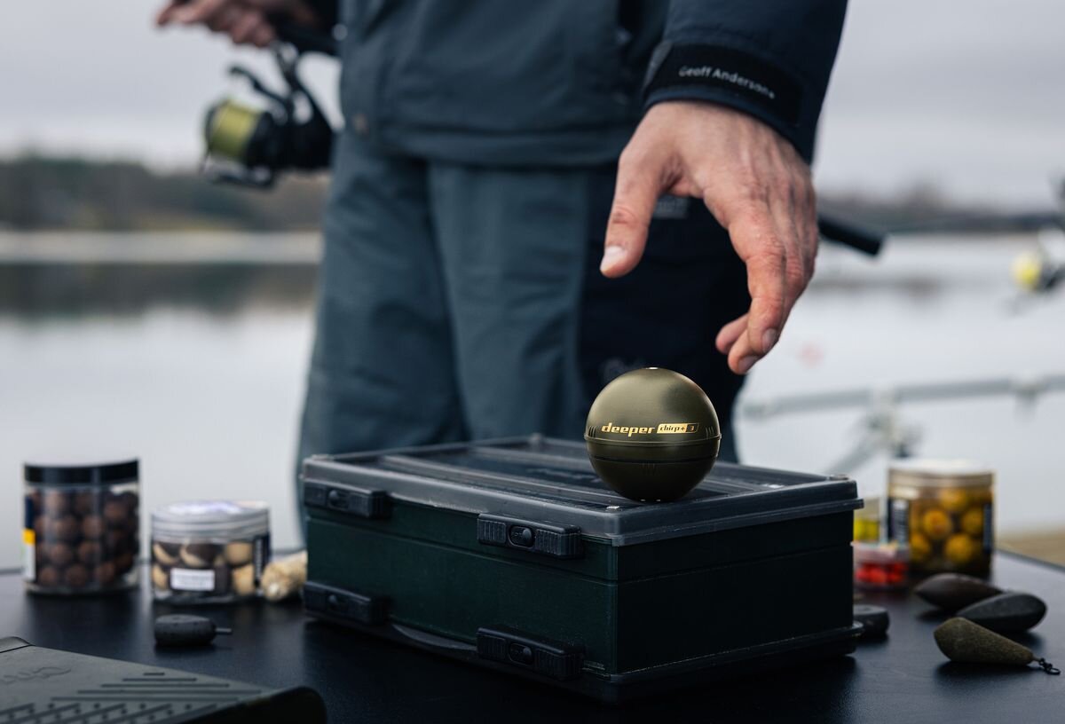 Echosonda wędkarska DEEPER CHIRP+ 3, 100m, zatoki, skany, wszechstronność, mężczyzna chwyta echosondę z blatu stołu kampingowego