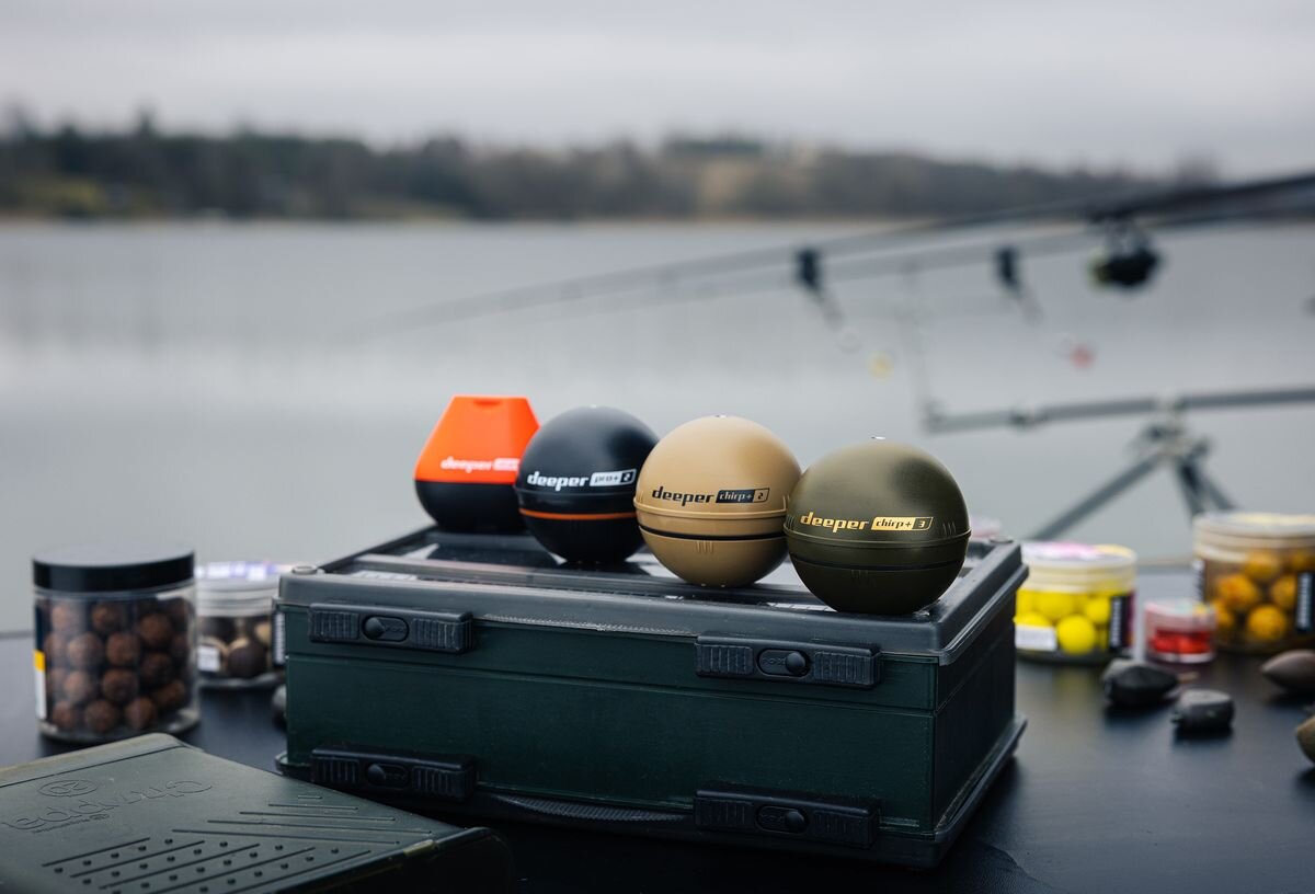 Echosonda wędkarska DEEPER CHIRP+ 3, nocne, osłona, spinning, czytelność, komplet echosond na stole kampingowym, w tle wędki przy brzegu jeziora