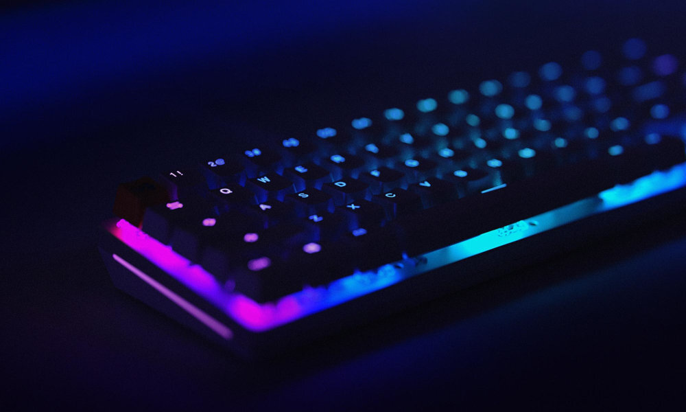 GLORIOUS GMMK2 Glorious GMMK 2 Compact gniazda „hot swap” bez potrzeby lutowania klawisze mechaniczne z 5 pinami fabrycznie nasmarowanymi przełącznikami Glorious Fox podświetlenie RGB nakładki na klawisze Glorious GMMK 2 65% - Klawiatura na biurku z kolorowym podświetleniem RGB, widok z boku w ciemnym otoczeniu