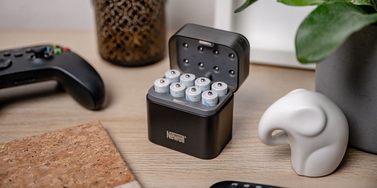 Akumulator NEWELL Li-ion AA 2200 mAh (4 szt.), Osiem białych akumulatorów AA umieszczonych w otwartej, czarnej ładowarce marki Newell na jasnym biurku, 1,5V, 2200mAh, AA, kompatybilny