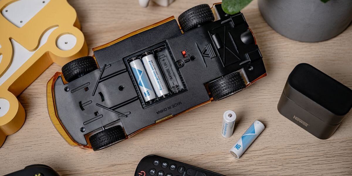 Akumulator NEWELL Li-ion AA 2200 mAh (4 szt.), Podwozie zabawkowego auta z dwiema bateriami AA w środku. Obok leżą dwa akumulatory i czarna ładowarka, 3,3Wh, samorozładowanie, Stałe1,5V, wydajność