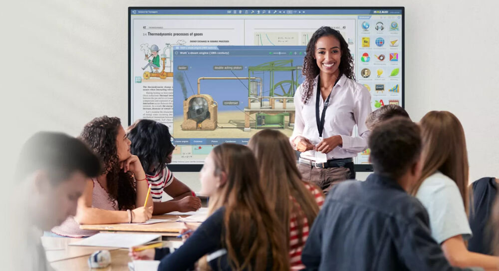 Monitor PRESTIGIO SOLUTIONS PMB000L864 86 cali 3840x2160px IPS monitor w sali lekcyjnej dzieci przy biurkach nauczycielka prowadząca lekcję przed monitorem interaktywna tablica 4K z ekranem 86 cali i technologią dotykową