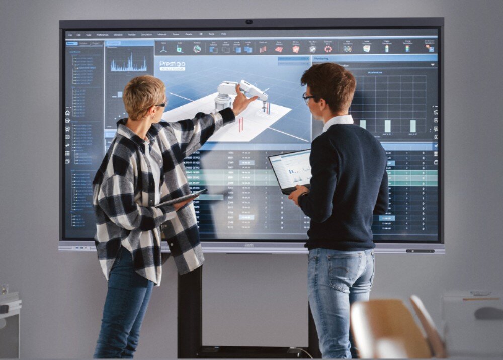 Monitor PRESTIGIO SOLUTIONS PSMB068P860 kobieta i mężczyzna stoją przy dużym ekranie interaktywnym, na którym wyświetlany jest projekt ramienia robotycznego oraz liczne dane techniczne i wykresy, opis