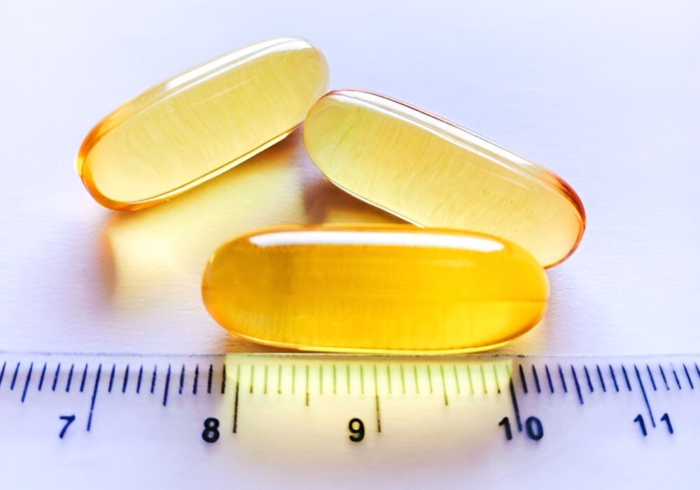 Suplement dla psa GAME DOG Omega-3 (60 kapsułek) Trzy złociste kapsułki żelowe z olejem rybim Omega-3 ułożone obok linijki pokazującej rozmiar około 2 centymetrów.