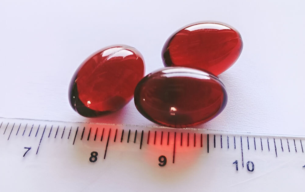 Suplement dla psa GAME DOG Krill Oil kwasy omega-3 EPA DHA zdrowe stawy serce układ krążenia Trzy czerwone, żelowe kapsułki oleju z kryla Game Dog obok linijki pokazującej rozmiar suplementu wynoszący około 2 cm.