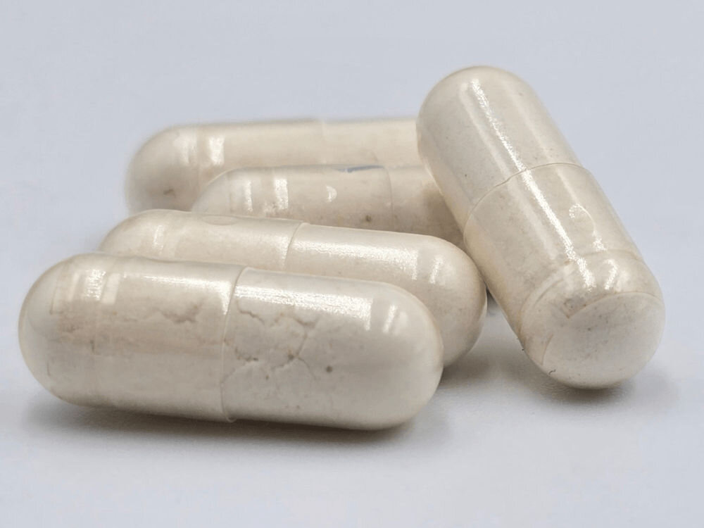 Suplement dla psa GAME DOG Flora Protect Probiotyk (60 kapsułek) Makro zbliżenie na pięć beżowych kapsułek suplementu Flora Protect ułożonych na jasnym tle. Kapsułki są półprzezroczyste i widoczna jest w nich proszkowa zawartość.