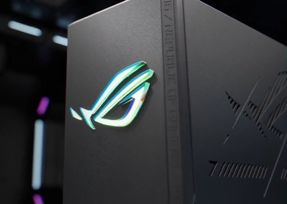 Router ASUS ROG Strix GS-BE18000 Zbliżenie na błyszczące, opalizujące logo na matowej, ciemnej obudowie, z widocznymi w tle rozmytymi kolorowymi światłami, pasma, funkcje