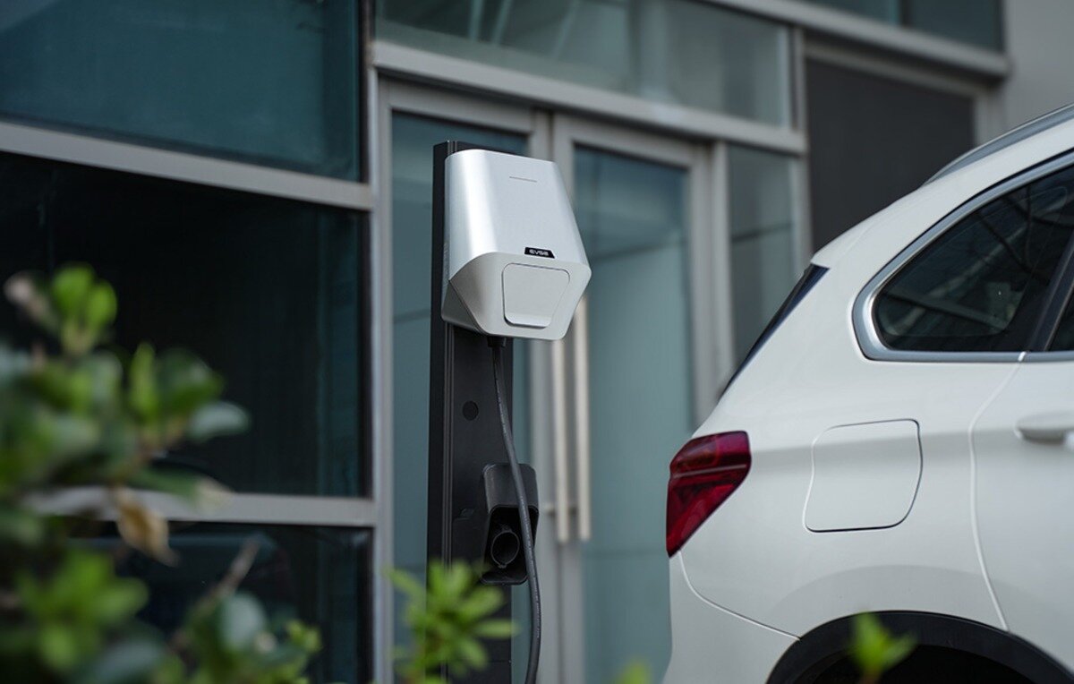 Ładowarka do samochodu elektrycznego BESEN LX30 App 22 kW Srebrna ładowarka samochodowa EVSE zamontowana na wolnostojącym słupku obok białego auta.