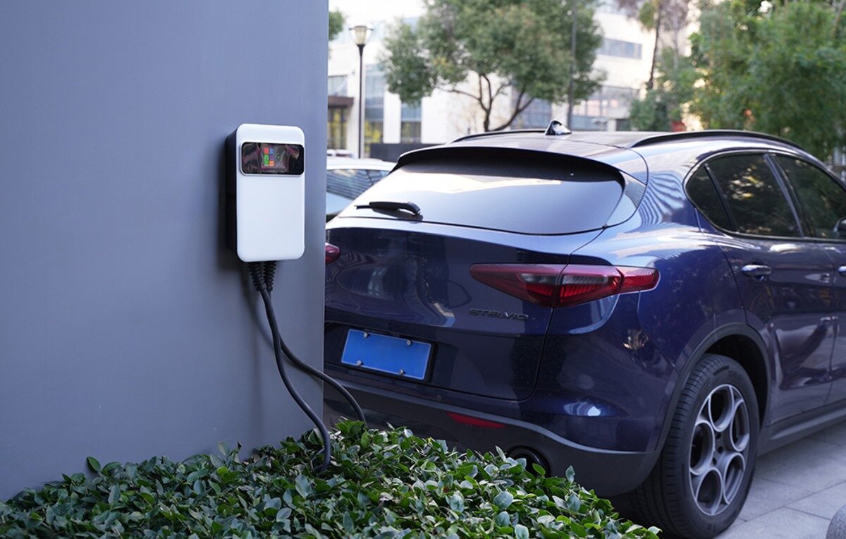 Ładowarka do samochodu elektrycznego BESEN SQ20 App 22 kW Biała ścienna ładowarka samochodowa z wyświetlaczem LCD zamontowana na szarym filarze obok granatowego Alfa Romeo Stelvio.
