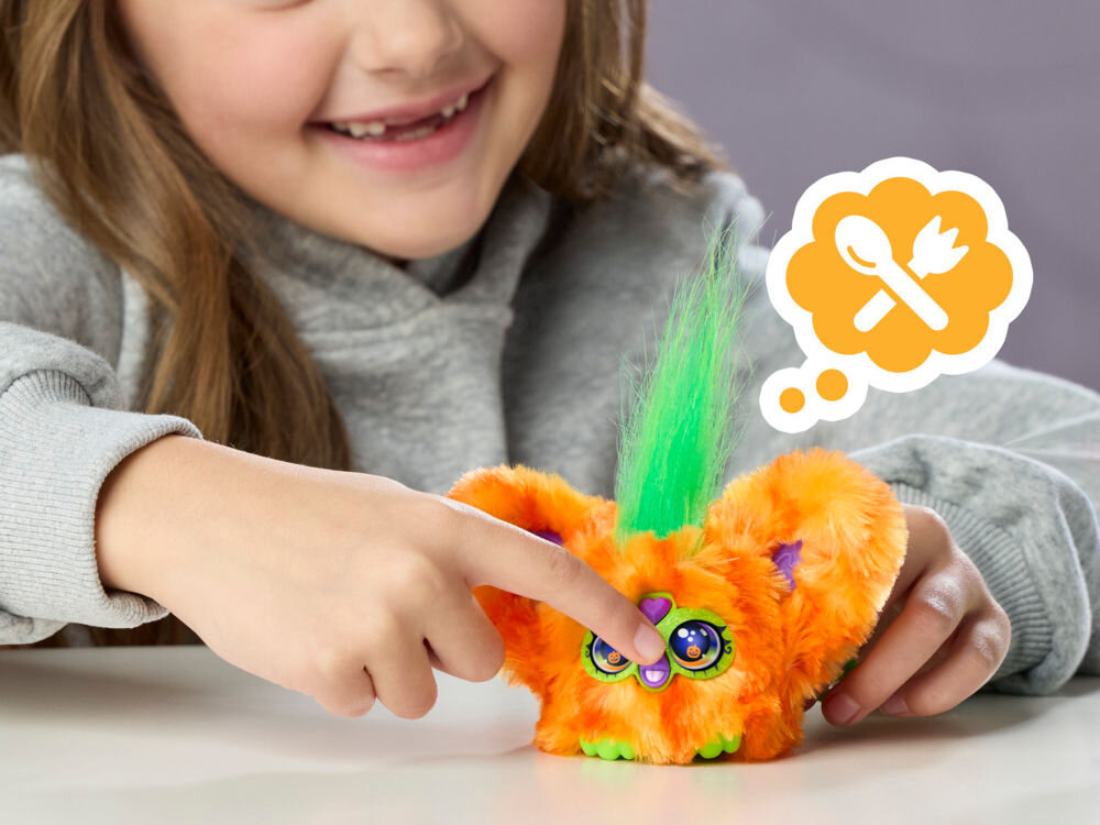 Maskotka HASBRO Furby Furbisie Boo-Kin G14355D0 Dziewczynka naciska palcem dziób pomarańczowej maskotki Furby Furblets. Nad zabawką znajduje się ikona w chmurce przedstawiająca sztućce, co sugeruje funkcję karmienia interaktywnego stworka.