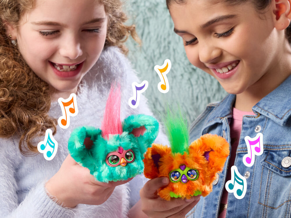 Maskotka HASBRO Furby Furbisie Boo-Kin G14355D0 Dwie dziewczynki bawią się wspólnie maskotkami Furby Furblets, zbliżając je do siebie. Kolorowe nutki na zdjęciu podkreślają muzyczny charakter zabawy.