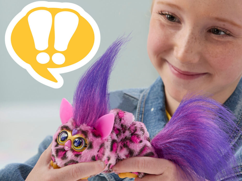 Maskotka HASBRO Furby DJ Furblets Kitt-Ee-Luv G17855X0 Uśmiechnięta dziewczynka trzyma w dłoniach interaktywną maskotkę Furby Furblets Ray-Vee w różowe cętki z fioletową czupryną.