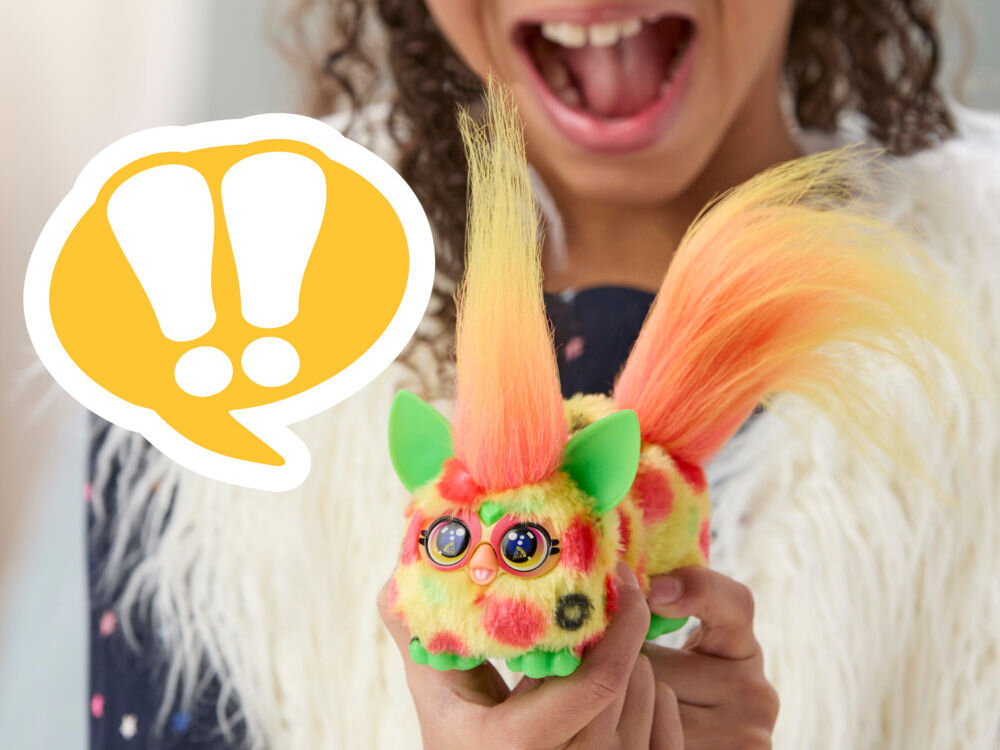 Maskotka HASBRO Furby DJ Furblets Pepp-Oh-Roni G17845X0 Uśmiechnięte dziecko trzyma w dłoniach małą, interaktywną maskotkę Furby Furblets Mello-Nee w żółto-czerwone wzory z pomarańczową czupryną.