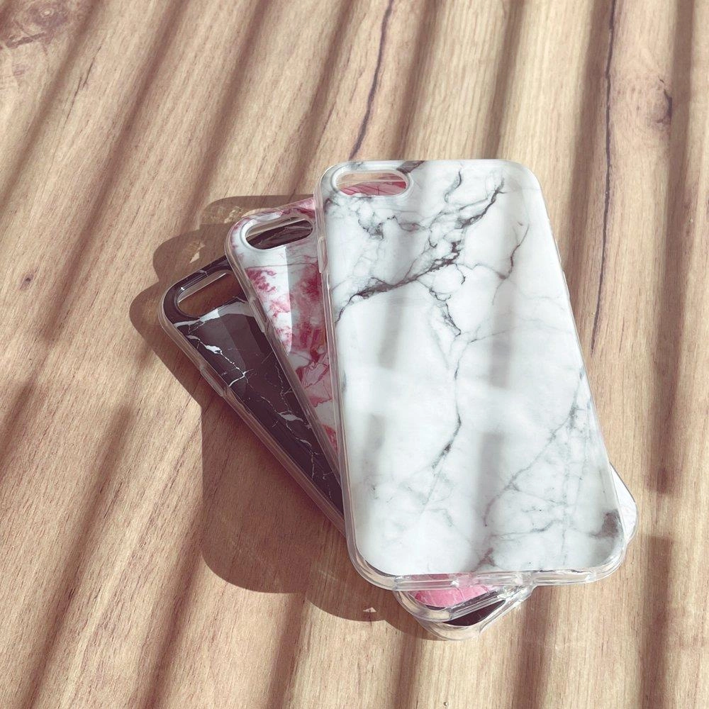Na drewnianej powierzchni leżą trzy żelowe etui na telefon z marmurowym wzorem w kolorach białym, czarnym i różowym.