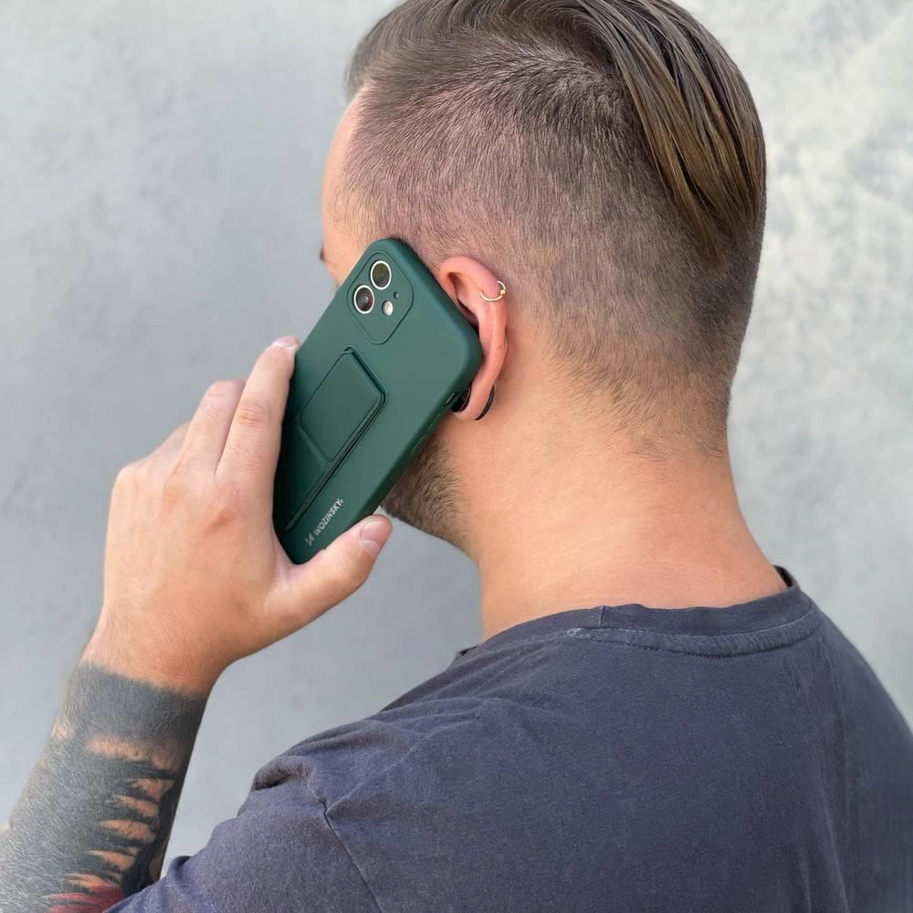 Osoba trzyma telefon z zielonym etui z podstawką przy uchu. Na etui widoczne jest logo \'Wozinsky\'.