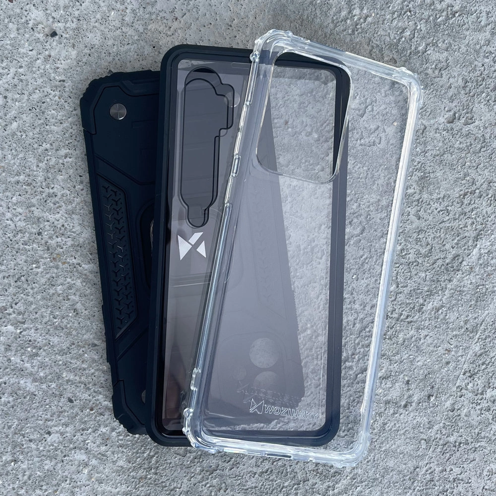 Na betonowej powierzchni leżą dwa etui na telefon, jedno przezroczyste, a drugie czarne z widocznym logo \'Wozinsky\'.