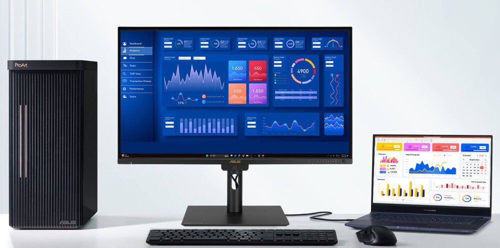 Na obrazie znajduje się monitor z wyświetlonymi wykresami i danymi, obok niego stoi komputer stacjonarny z napisem \'ProArt\' oraz laptop z podobnymi wykresami. Przed monitorem znajduje się klawiatura i myszka.