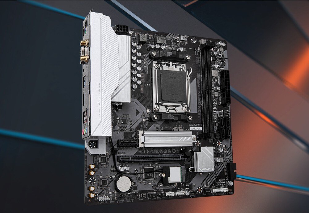 Płyta główna GIGABYTE B650M Gaming WiFi6E Zdjęcie płyty głównej komputera w formacie micro-ATX, pokazane pod kątem na tle niebieskich i pomarańczowych pasów. Widoczne są srebrne radiatory sekcji zasilania i chipsetu, gniazdo procesora oraz dwa banki pamięci RAM