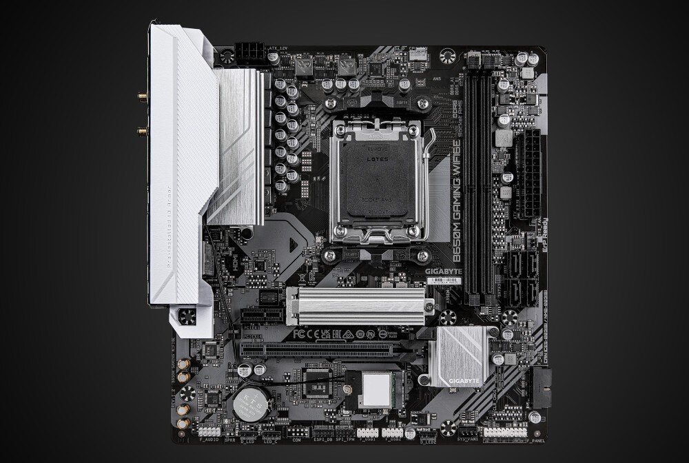 Płyta główna GIGABYTE B650M Gaming WiFi6E Zdjęcie płyty głównej komputera wykonane z góry na jednolitym czarnym tle. Widoczny jest układ komponentów, w tym gniazdo procesora, sloty pamięci, gniazdo PCIe oraz złącza tylnego panelu z antenami Wi-Fi