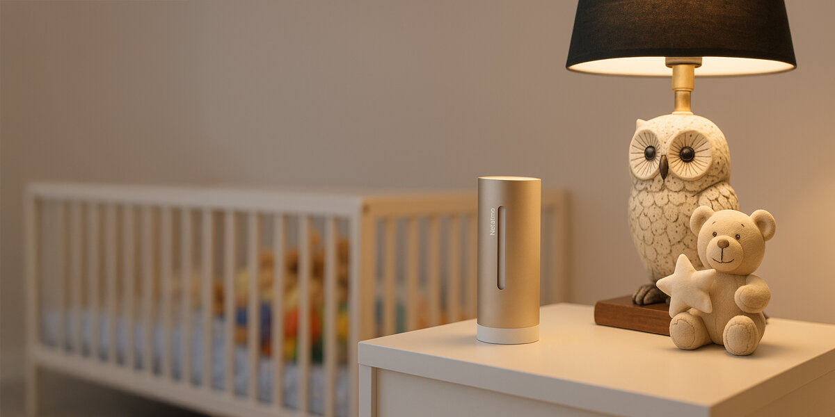 Moduł wewnętrzny Netatmo stoi na białej szafce nocnej obok lampki nocnej w kształcie sowy i pluszowego misia.