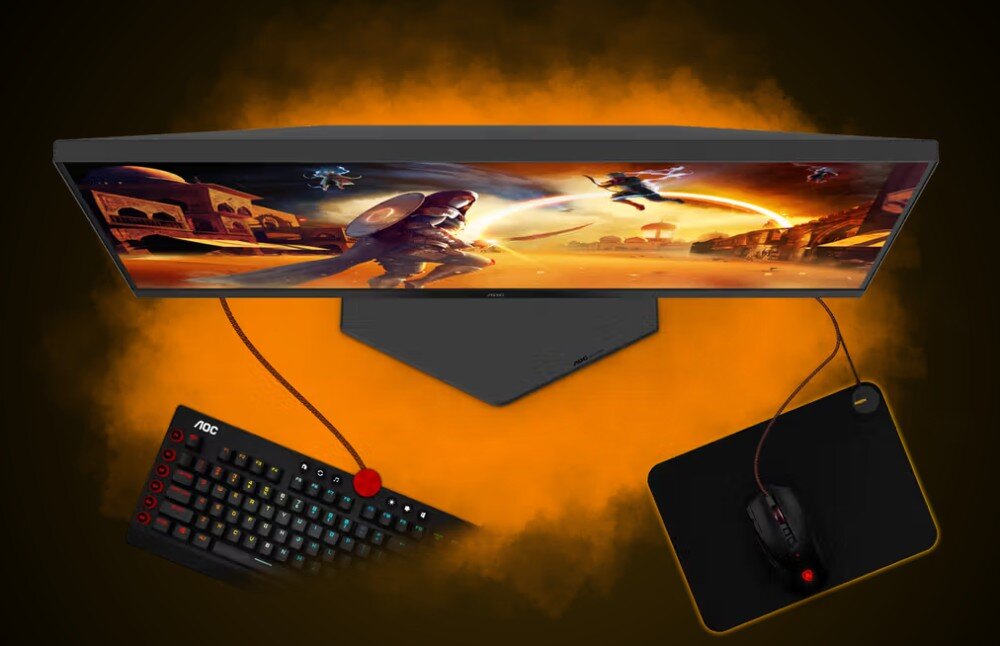 Obraz przedstawia monitor z dynamiczną sceną z gry, klawiaturę z podświetleniem RGB z logo \'AOC\' oraz myszkę na podkładce, wszystko na tle pomarańczowej poświaty.