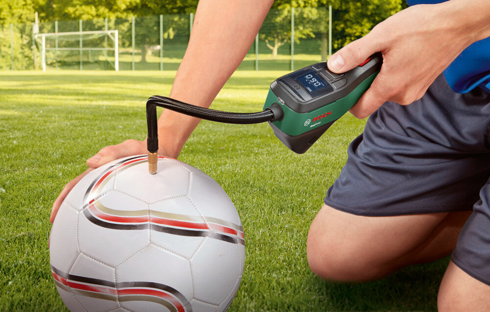 Pompka rowerowa BOSCH EasyPump 2 0603947001 trawnik osoba pompuje piłkę do nogi w tle bramka drzewa wbudowany akumulator 3,6 V o pojemności 3,0 Ah złącze USB-C mobilność swoboda działania w zestawie kabel USB-A/USB-C wskaźnik poziomu naładowania