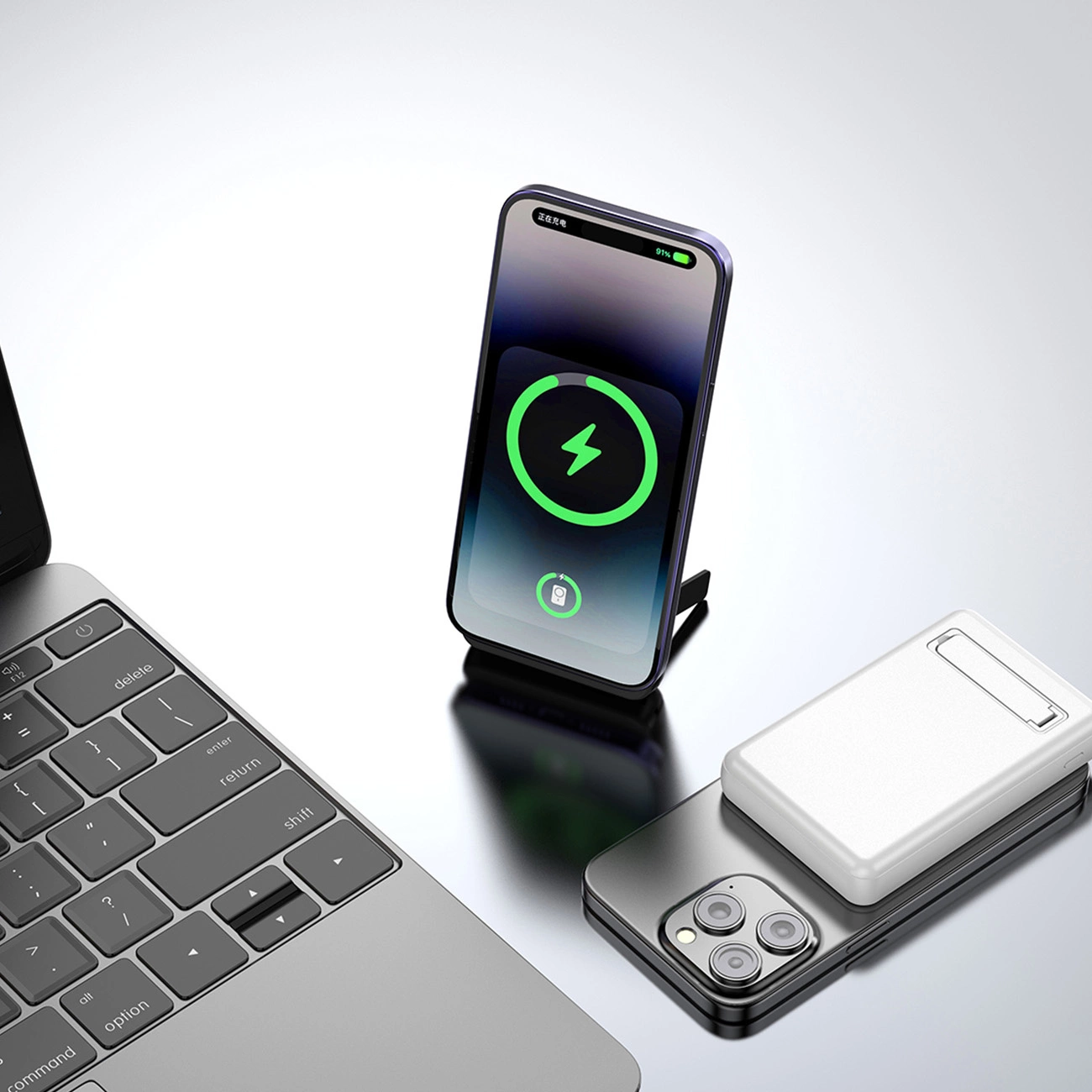 Na obrazie widoczny jest biały powerbank umieszczony na smartfonie oraz laptop z widoczną klawiaturą. Obok znajduje się stojący smartfon z ekranem pokazującym ikonę ładowania.
