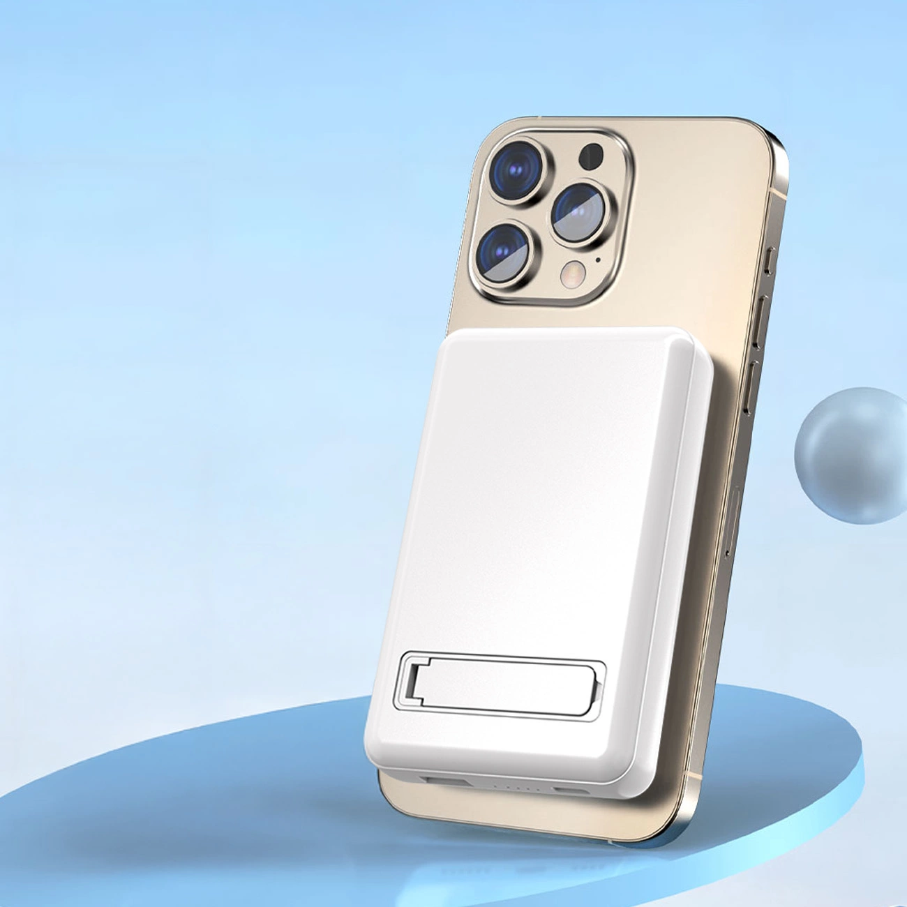 Na obrazie widoczny jest biały powerbank przymocowany do tylnej części złotego smartfona. W tle znajduje się niebieskie tło z delikatnym gradientem i unoszącą się kulą.