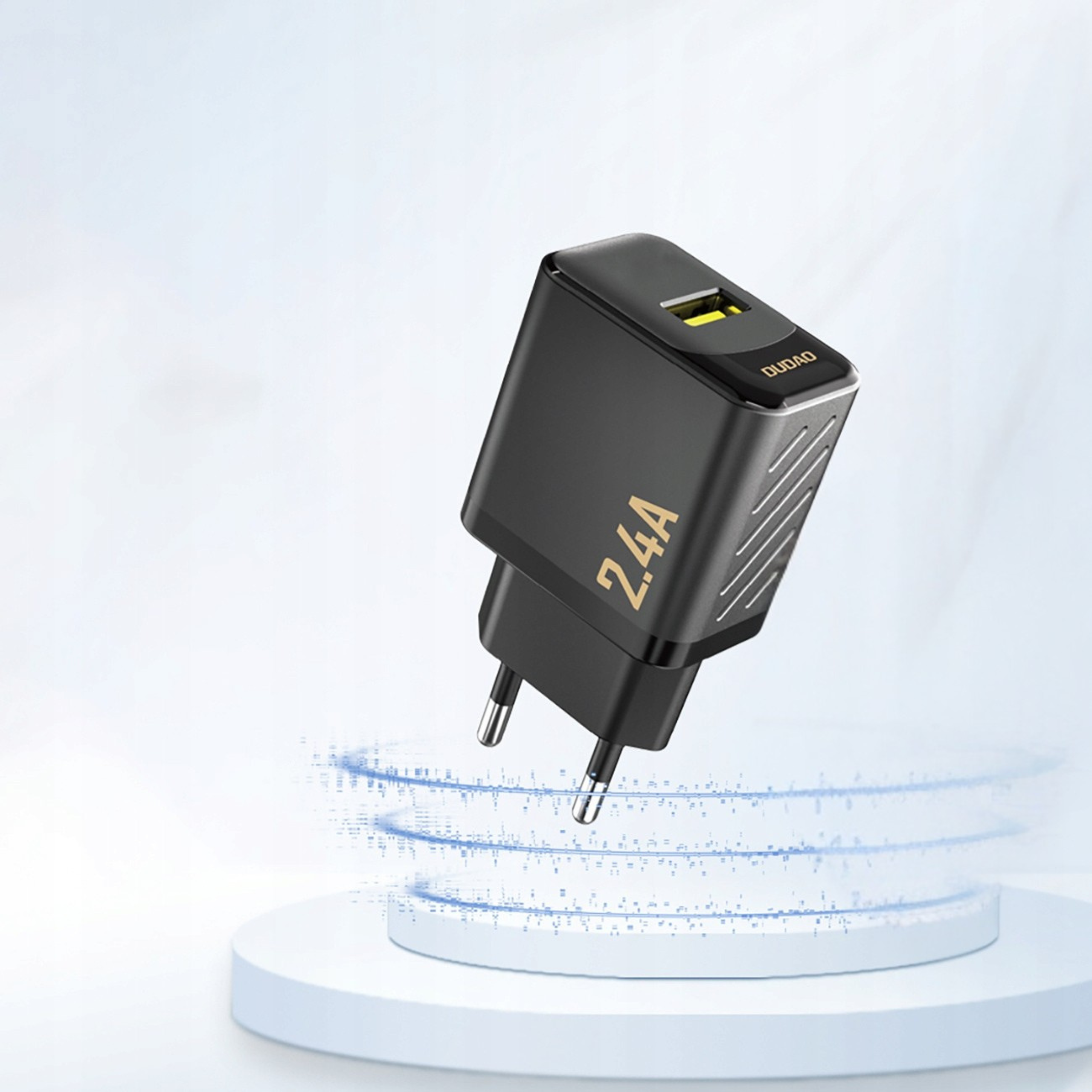 Czarna ładowarka z napisem \'2.4A\' i logo \'DUDAO\' na górze, z jednym portem USB-A. Ładowarka unosi się nad okrągłą, białą platformą na jasnym tle.