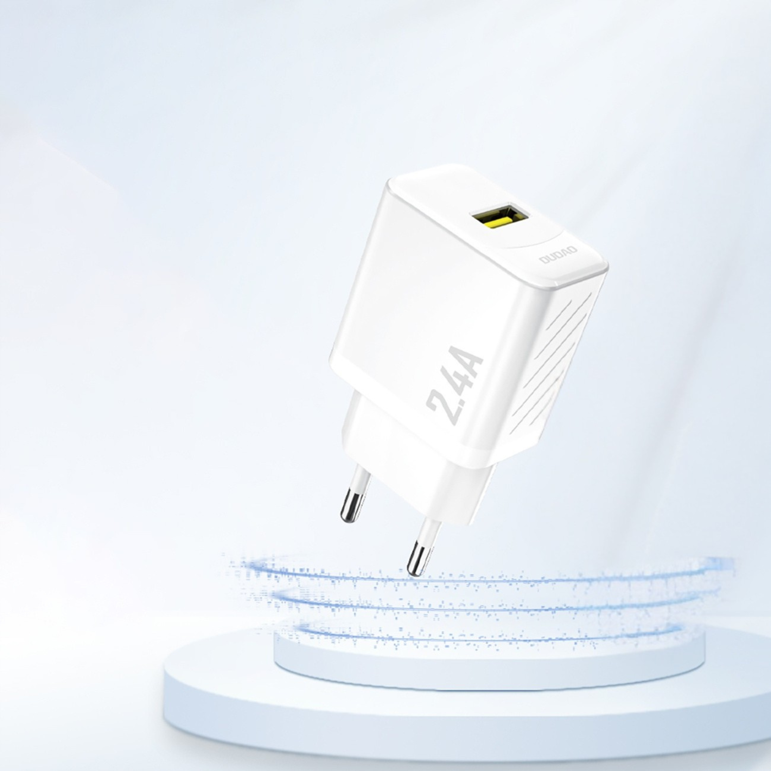 Biała ładowarka z napisem \'2.4A\' i logo \'DUDAO\' na górnej części, z jednym portem USB-A. Ładowarka unosi się nad okrągłą podstawą na jasnym tle.