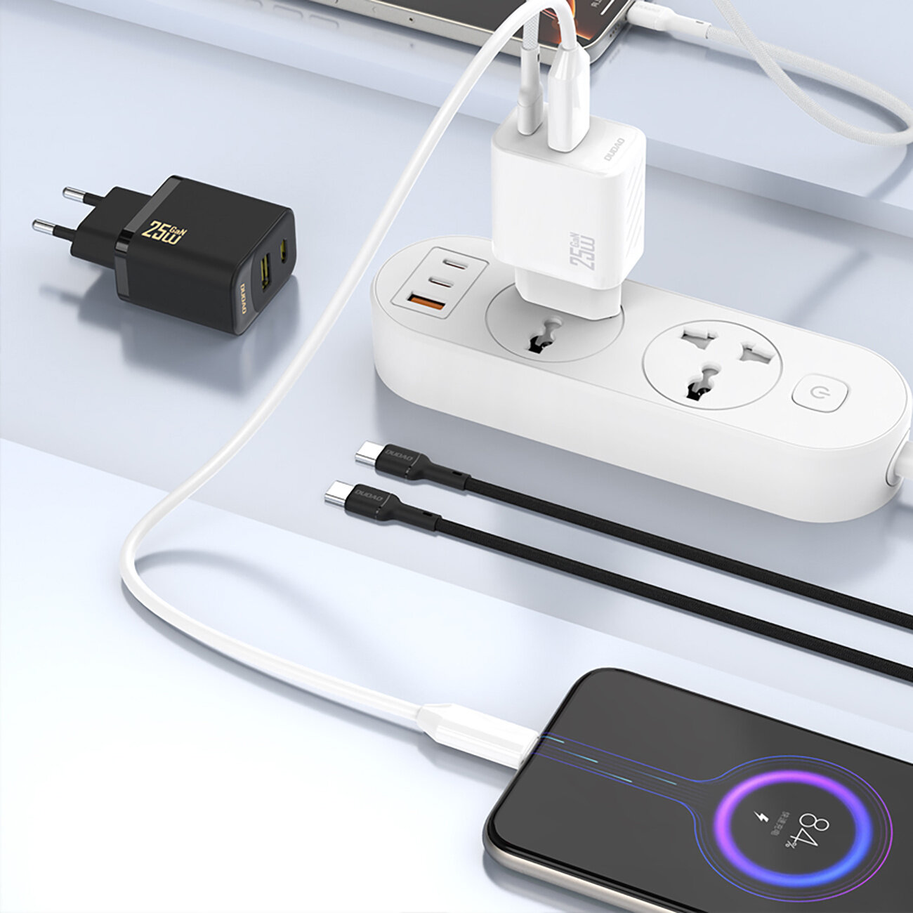 Na obrazie widoczna jest czarna ładowarka sieciowa z dwoma portami USB i oznaczeniem \'25W\'. Obok znajduje się biała listwa zasilająca z podłączonymi urządzeniami oraz dwa kable USB-C.