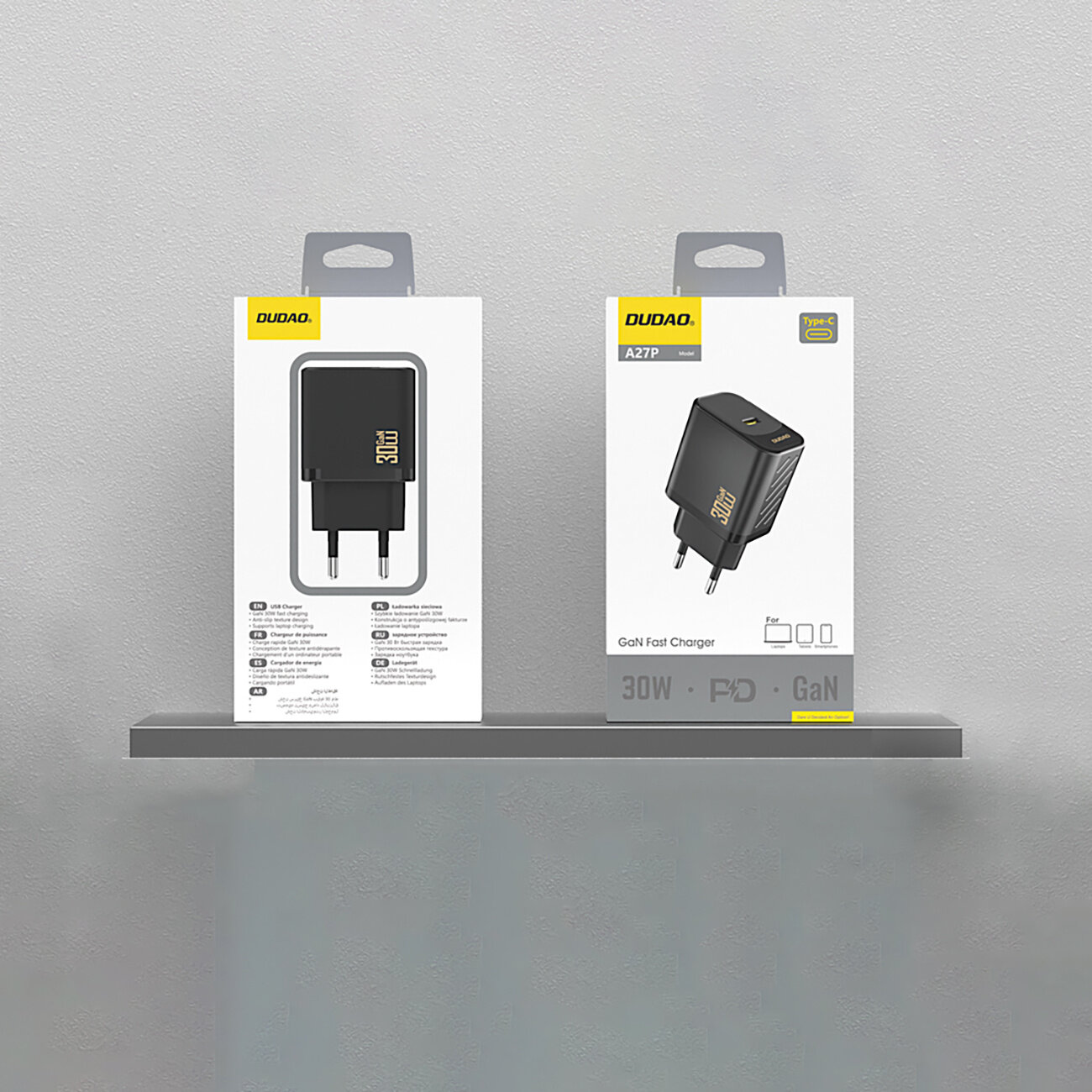 Na obrazie widoczne są dwa opakowania ładowarki sieciowej Dudao A27P 30W Pd GAN USB-C w kolorze czarnym, umieszczone na półce. Opakowania mają logo Dudao i zawierają zdjęcia produktu oraz informacje techniczne.