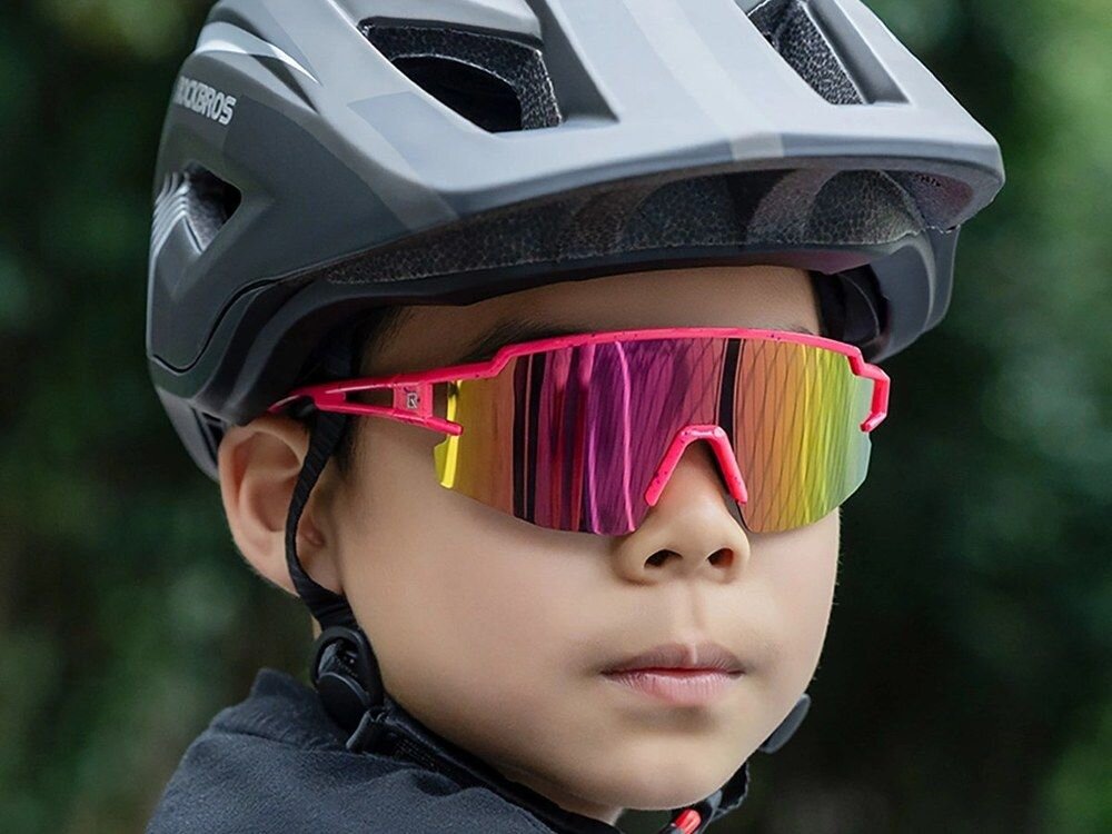 Osoba nosi różowe okulary rowerowe z lustrzanymi szkłami oraz szary kask z widocznym logo ROCKBROS.