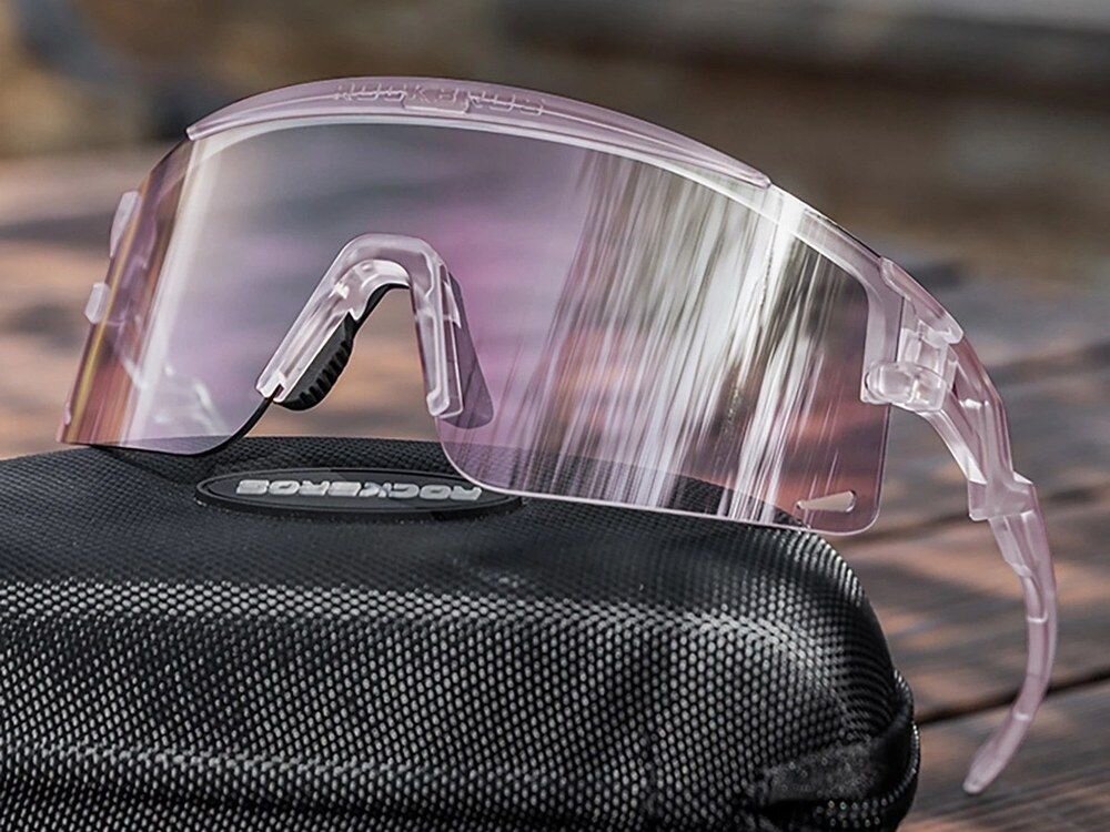 Fioletowe okulary rowerowe z przezroczystymi soczewkami leżą na czarnym etui z logo \'ROCKBROS\'.