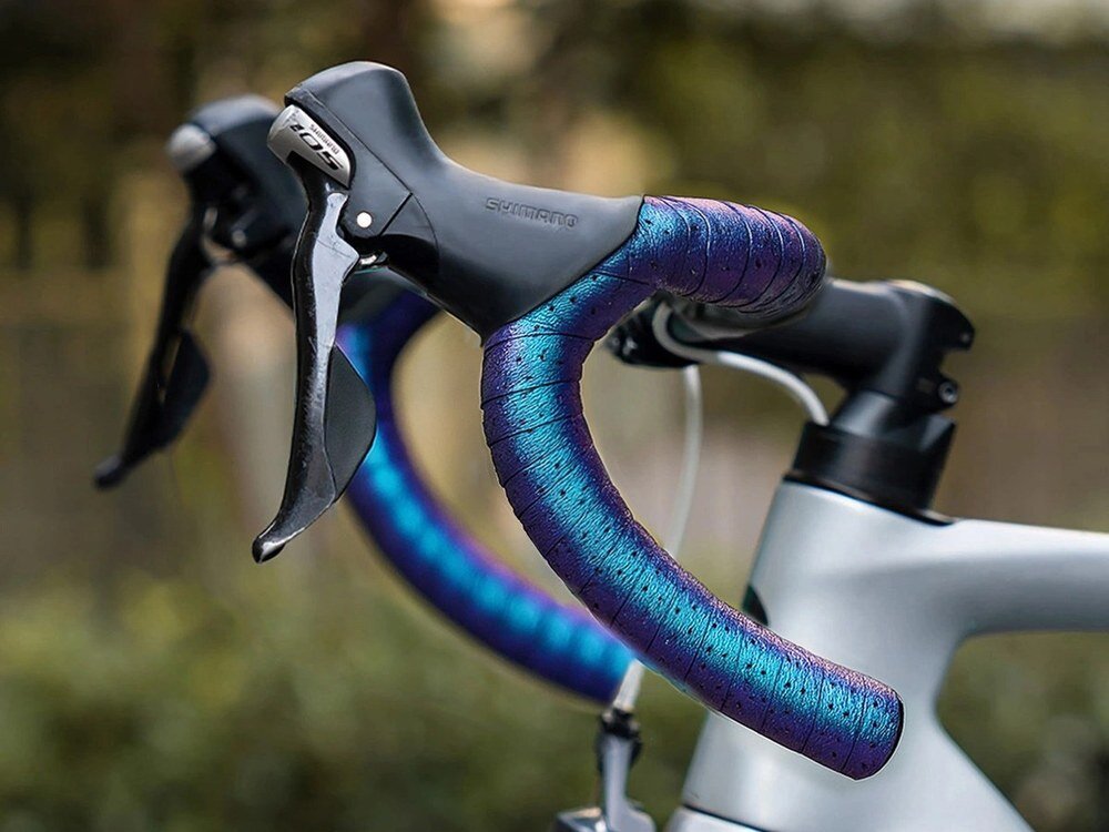 Rowerowa kierownica z owijką w kolorze fioletowym z niebieskimi akcentami. Na dźwigni hamulca widoczny jest napis \'Shimano\'.