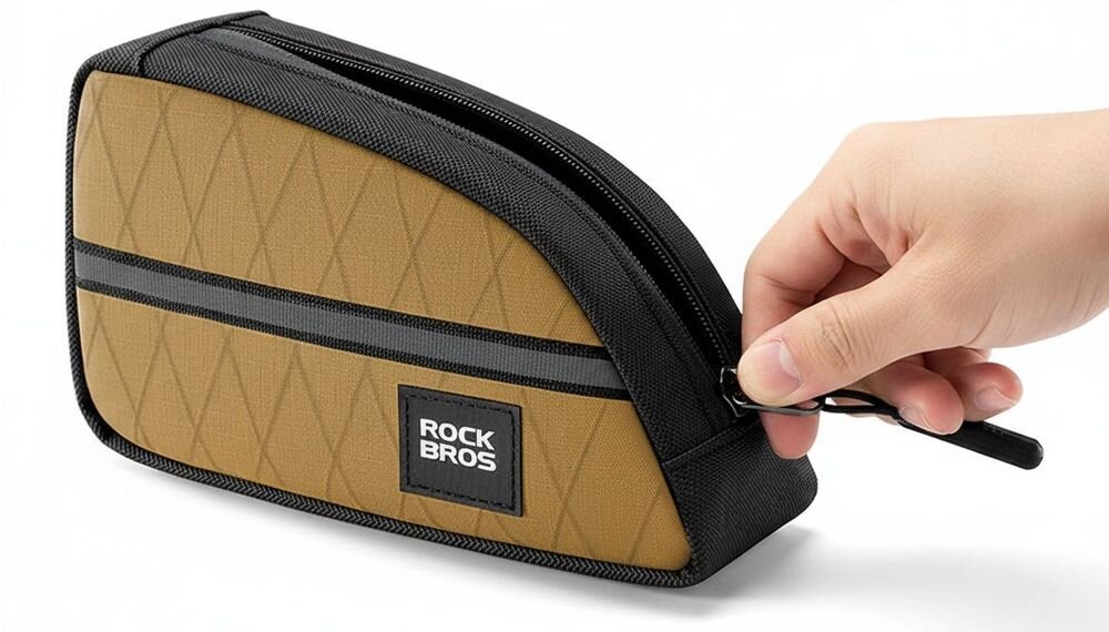 Brązowa torba rowerowa z czarnymi elementami i zamkiem błyskawicznym, trzymana przez rękę. Na torbie widoczne jest logo \'ROCK BROS\'.